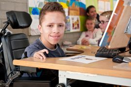 Computerende jongen achter aangepast tafel